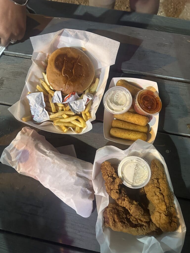  Burger, fries, chicken tenders and other fast food from Dem Smash Burger on a picnic table.