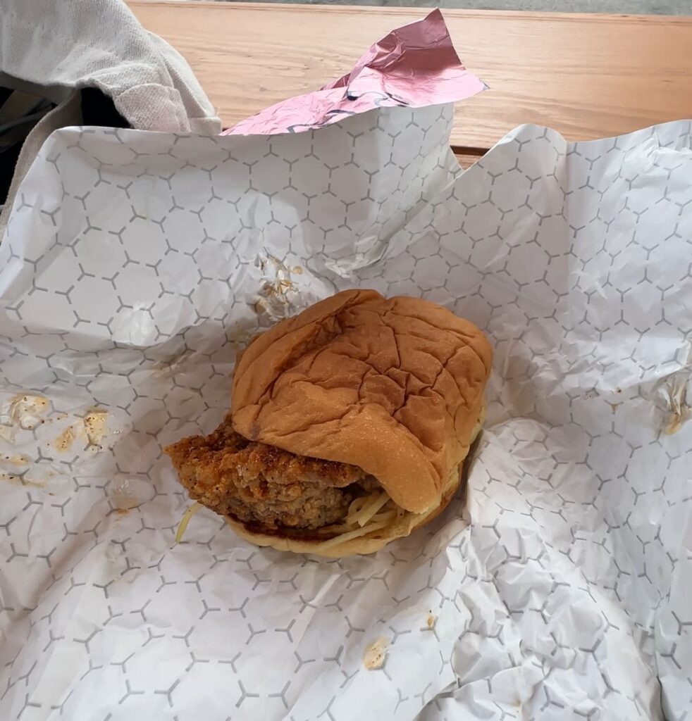 Original chicken sandwich from Spicy Boys Fried Chicken inside the wrapper on a picnic table