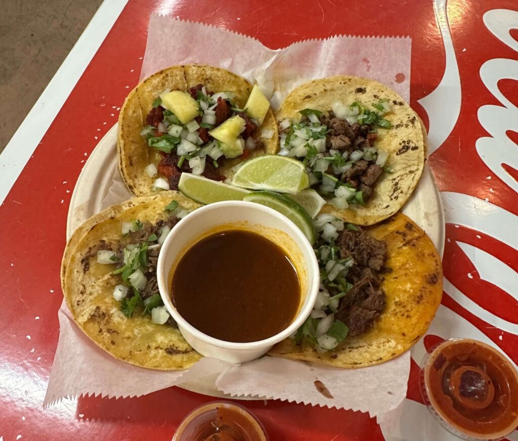 Four tacos with dipping sauce on red table at One Taco Taqueria